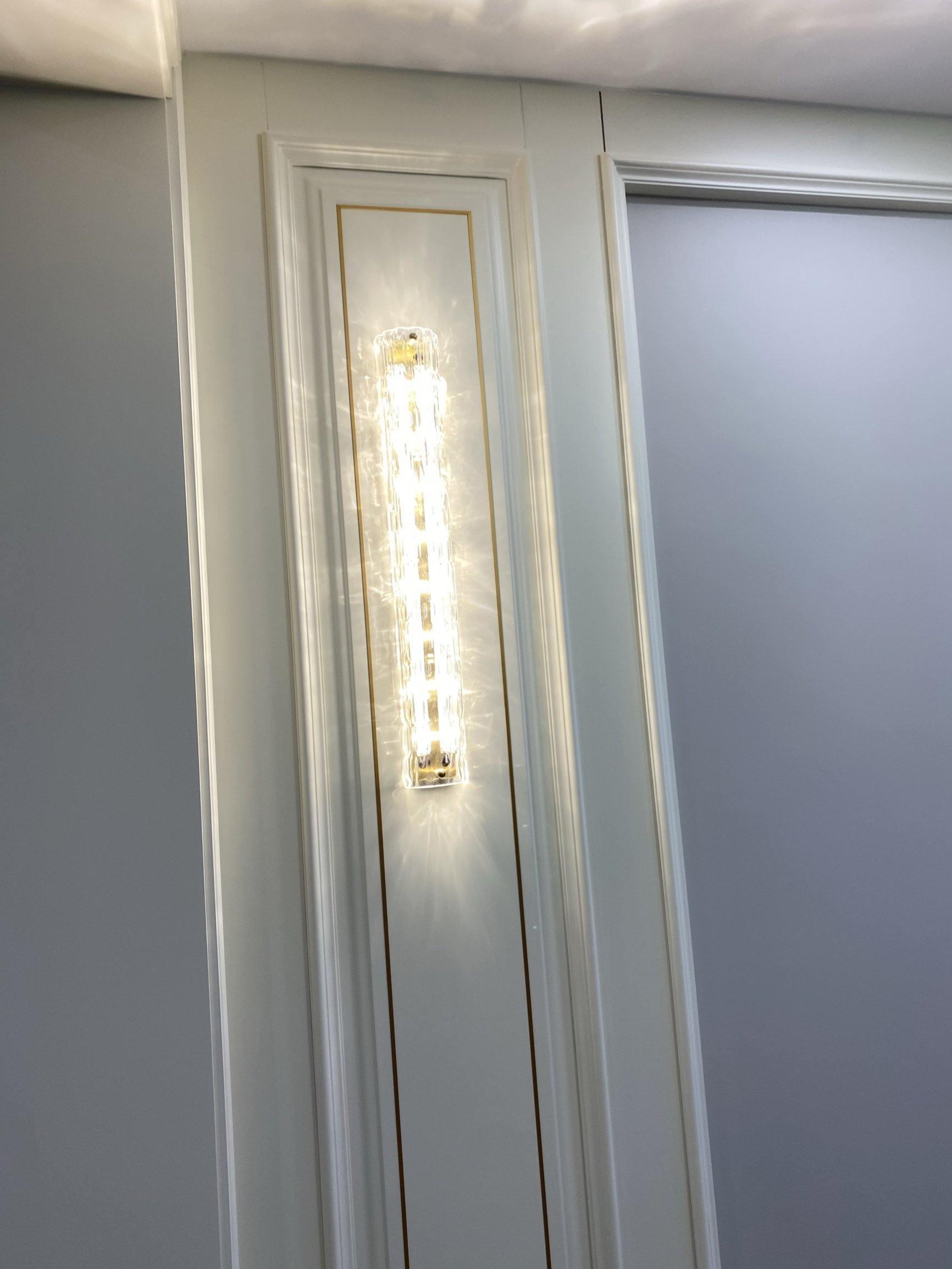 Warm-lit glass bar on pale panel beside roller blind
