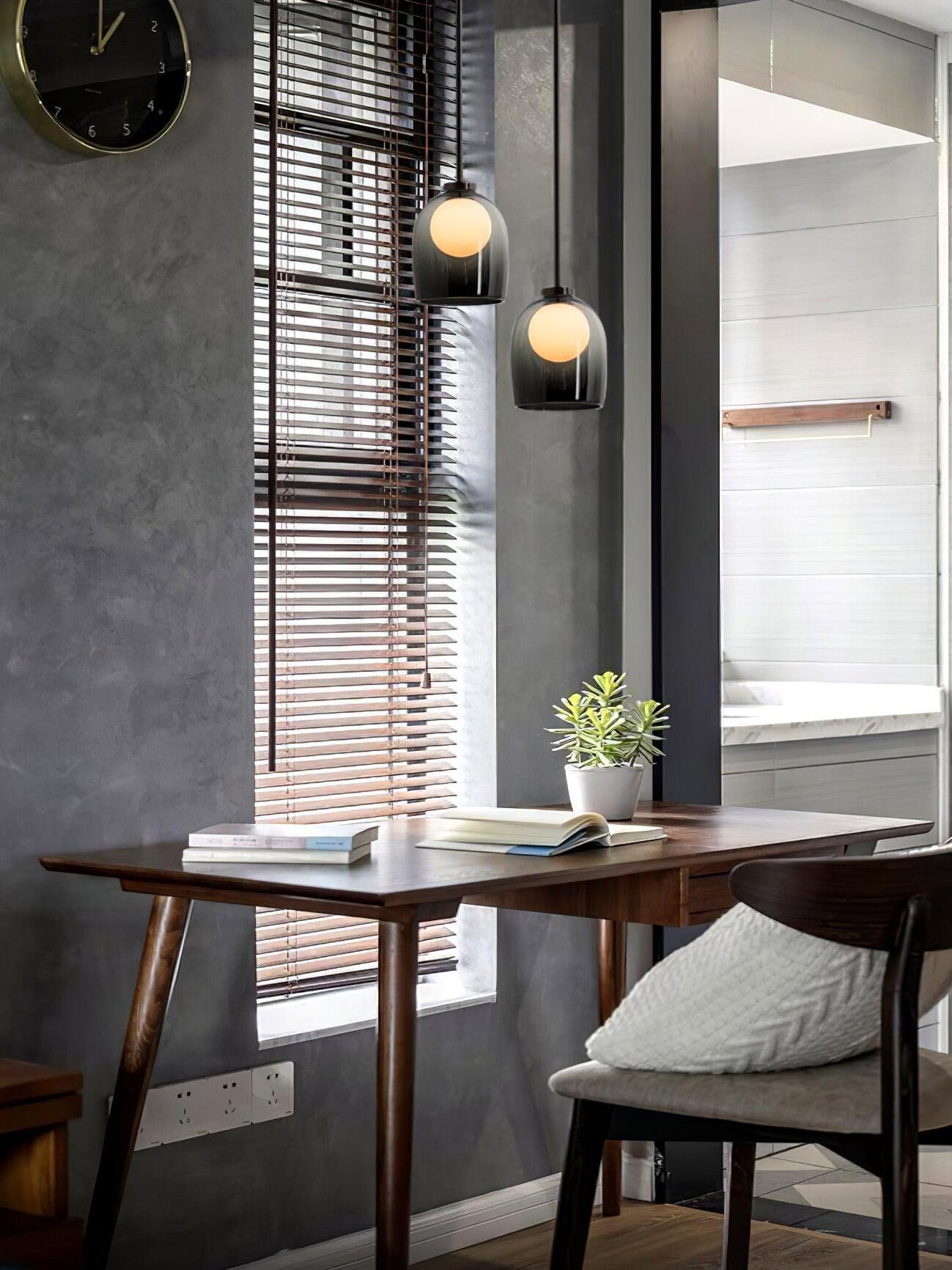 Two gradient-black Crux pendants at staggered heights above a table beside window blinds