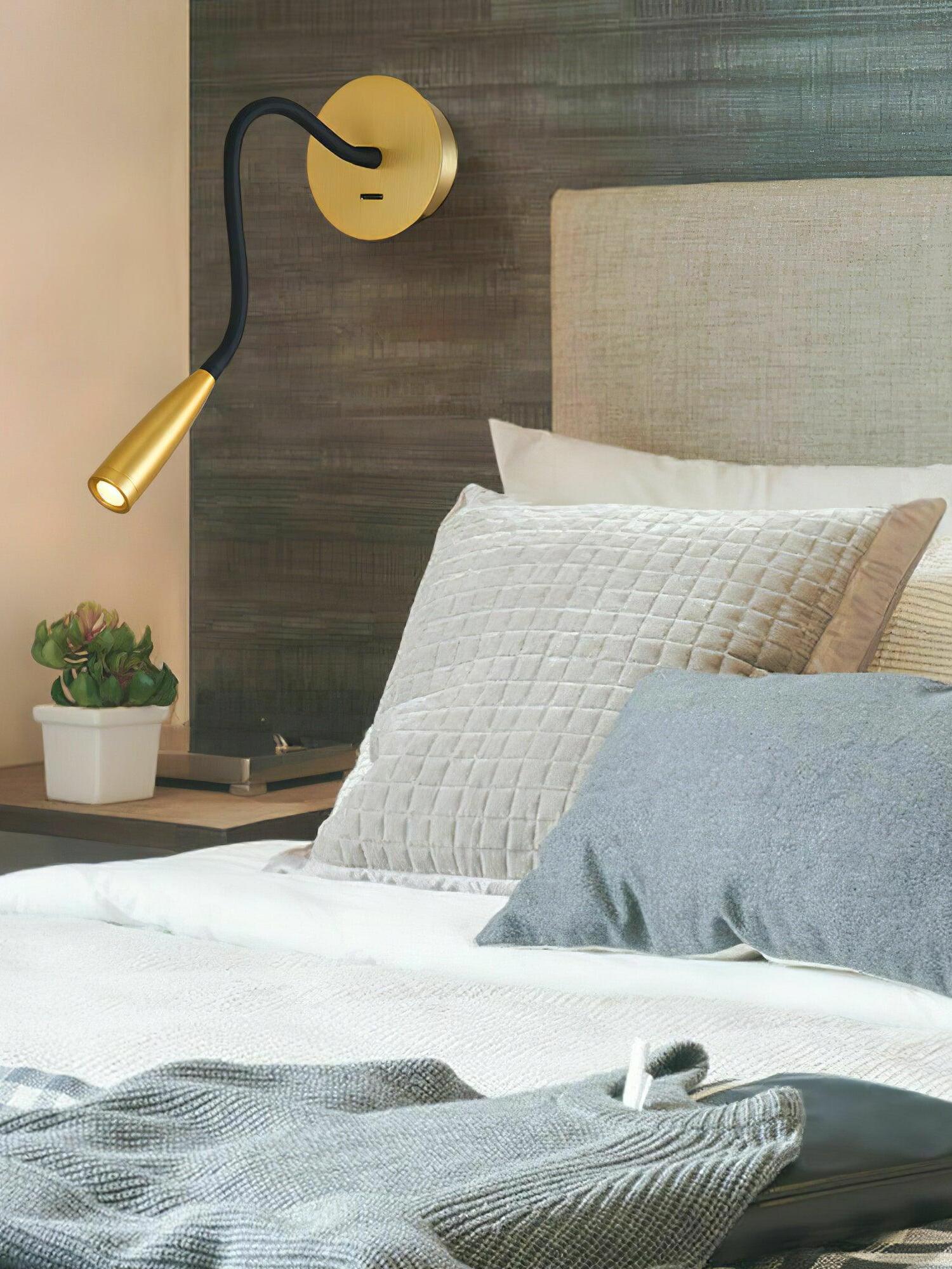 Gold Flexi beside a pale upholstered headboard and textured pillows, angled over a nightstand with flowers and books