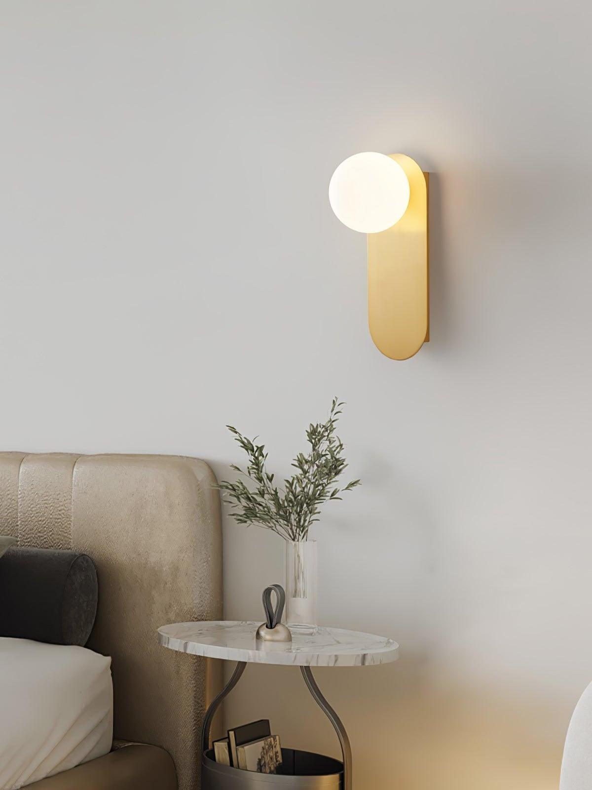 Brass globe sconce beside an upholstered bed and round side table