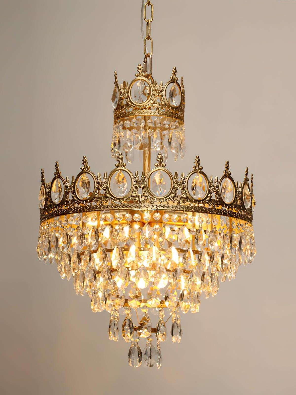 Illuminated crown-style crystal chandelier with a narrow upper disc and clear drops against a beige wall