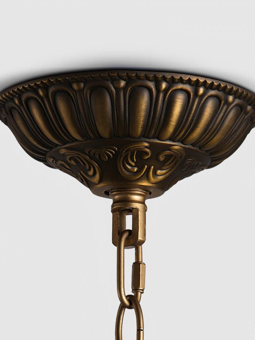 Round gold-tone ceiling canopy with a fluted edge, scroll motif and chain connector on a white background