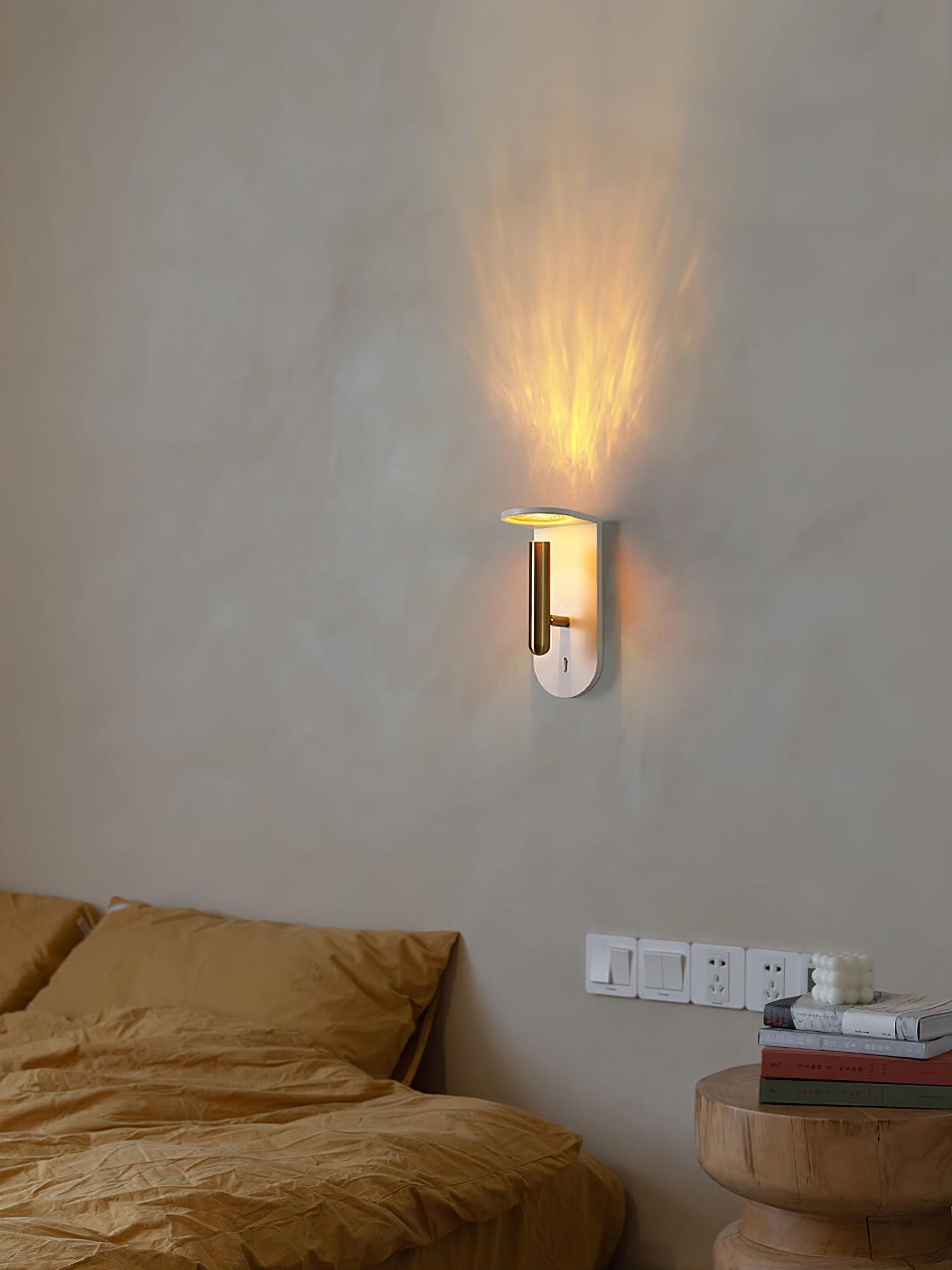 White Nights wall light on a grey wall above a bed with yellow bedding and a wooden bedside table