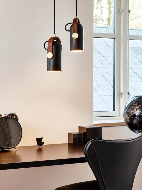 Two black wood-bracket pendant lights at staggered heights over a wooden desk beside a window, clock and globe