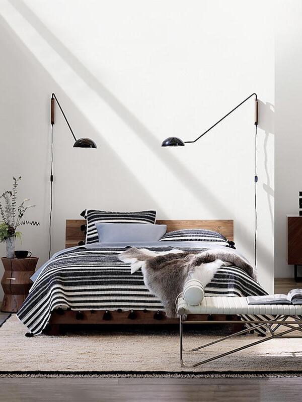 Two black dome wall lamps on separate wooden mounts beside a bed, each with a hanging switched cord