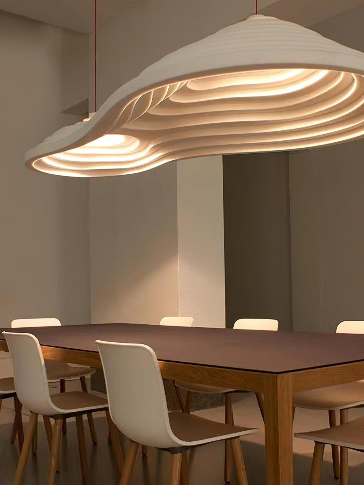 Underside of an elongated contoured pendant above a wooden table surrounded by pale chairs.