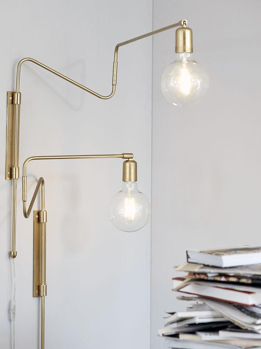 Two brass-tone wall lamps with bent arms, glowing globe bulbs and separate backplates beside books