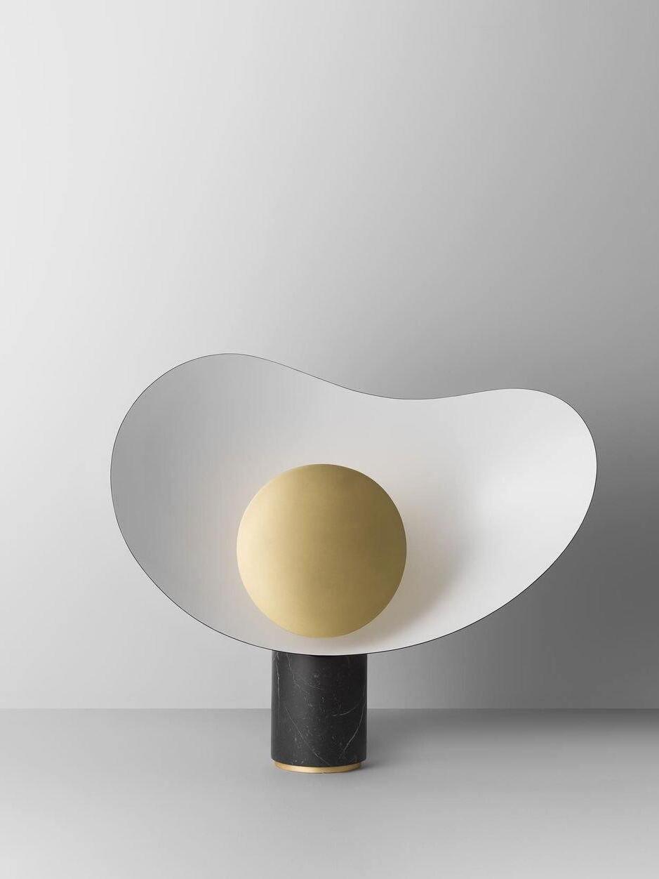 White sculptural lamp on black column against grey wall