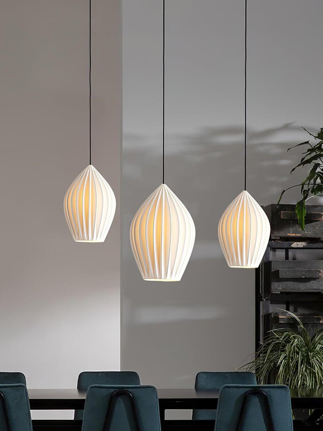 Three illuminated ribbed ceramic pendants above a dining table with dark chairs