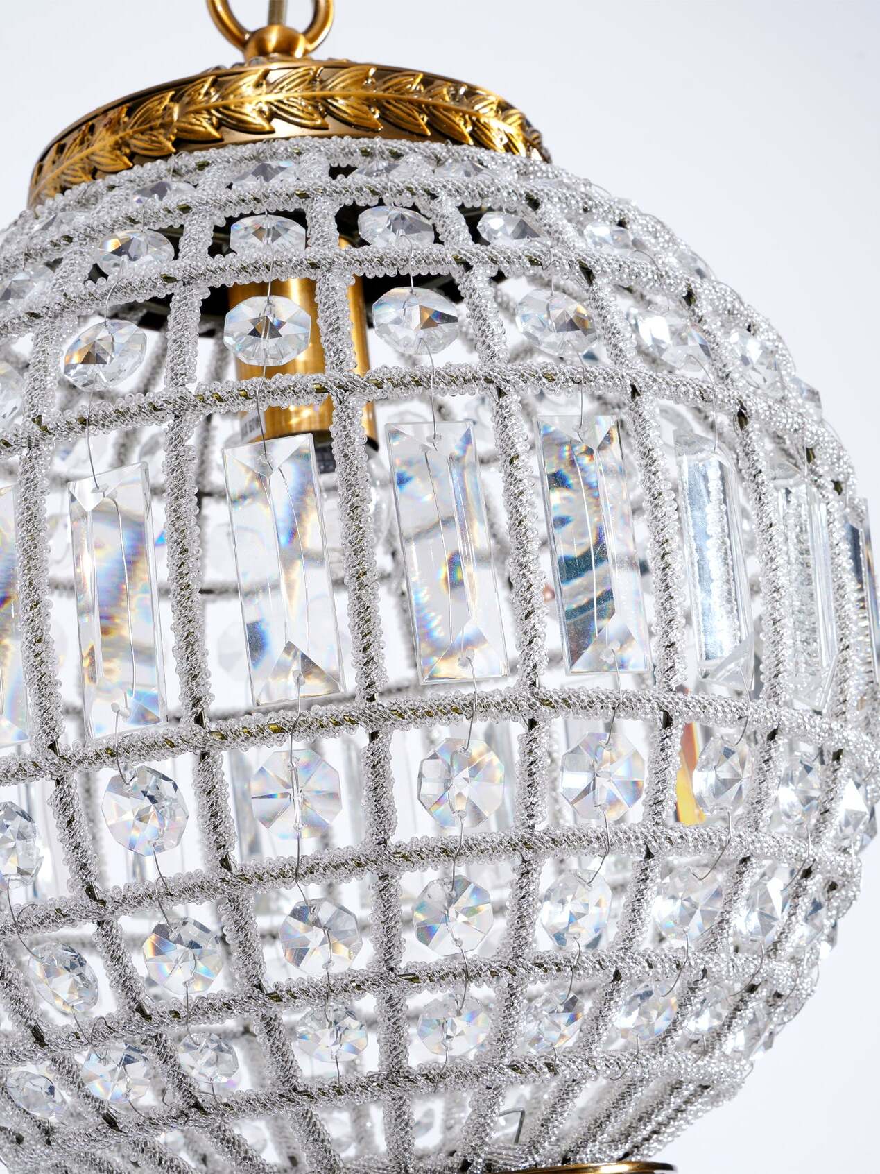 Close view of round faceted crystals, rectangular center pieces and beaded cage ribs beneath a gold-tone cap