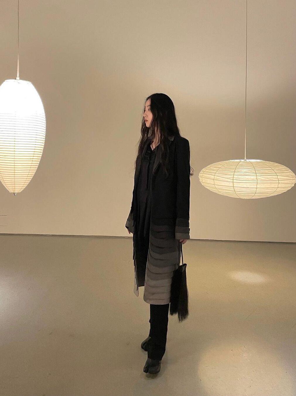 Person standing between an elongated paper lantern at left and a flattened paper lantern at right in a display room