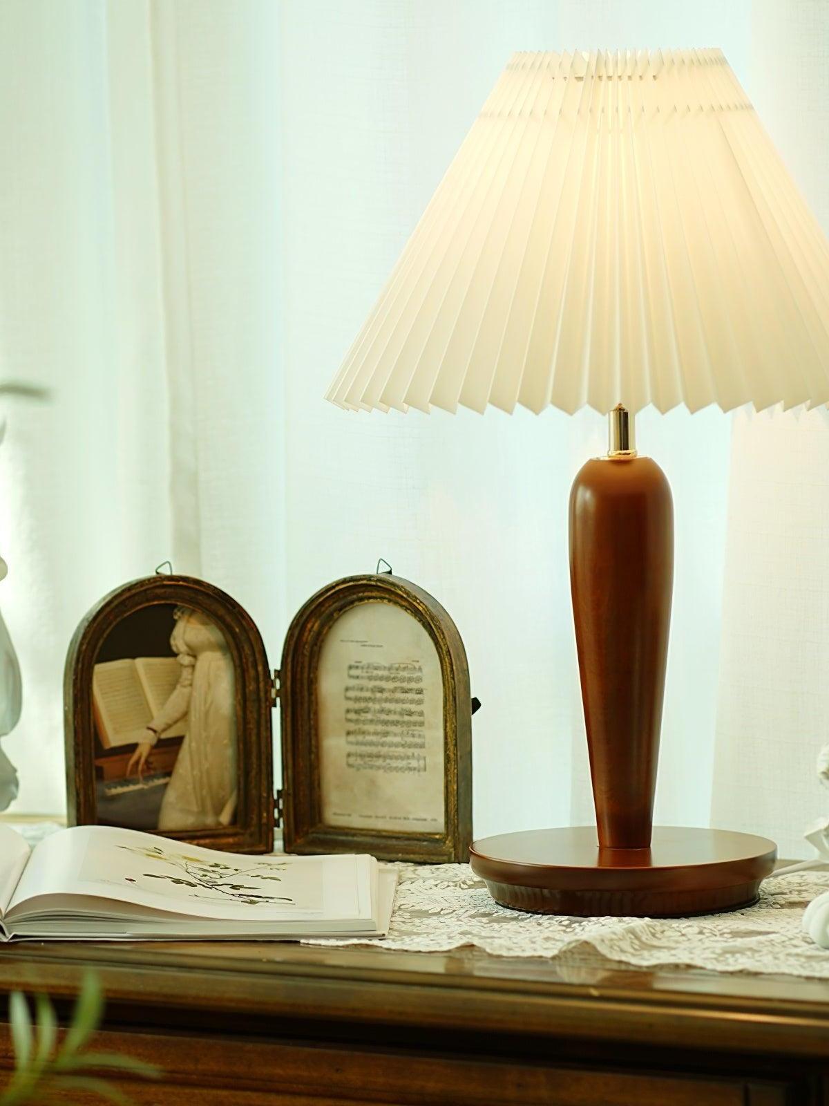 Brown lamp with glowing pleated shade among dresser objects