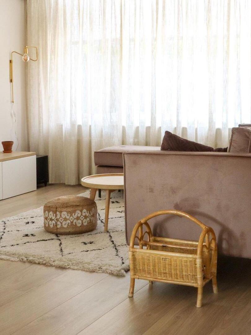 Brass-tone wall lamp in a bright living room with taupe sofa, sheer curtains and woven magazine basket