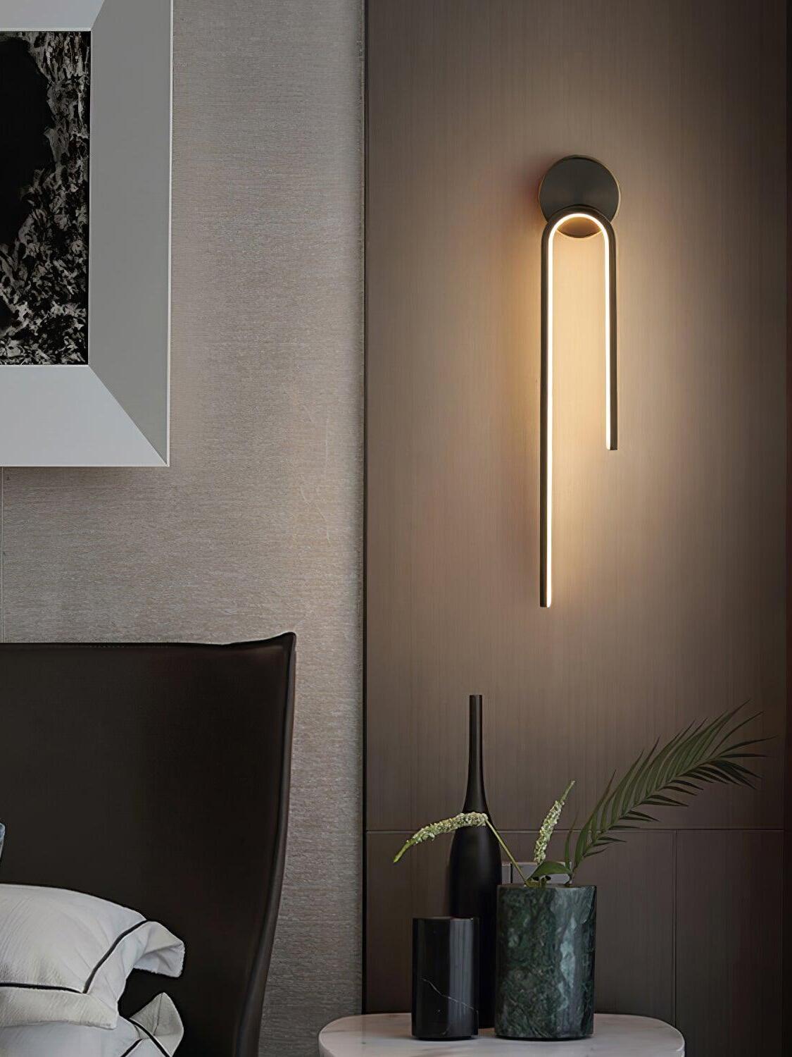 Dark arch with a long left arm above bedside vases and a plant beside framed artwork and a bed