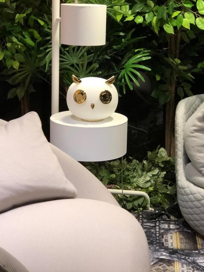 Owl lamp on circular white shelf beside seating, plants and shaded lamp