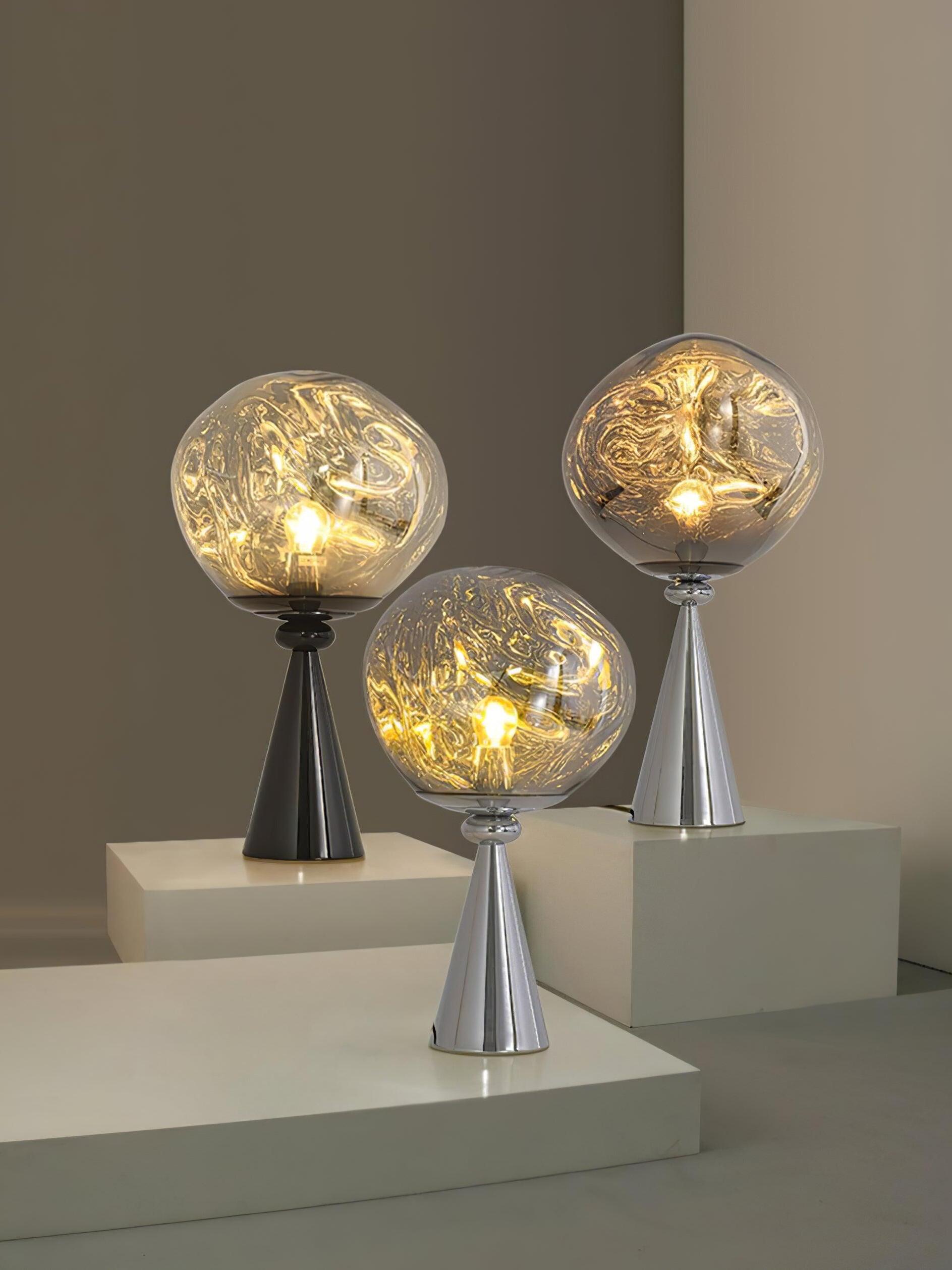 Three glowing globe table lamps with chrome or black cone bases on pale display blocks