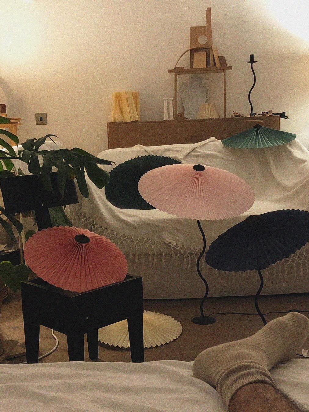 Styling scene of pleated shades in black, green, pink, orange and cream, with curved lamp stems and loose shades