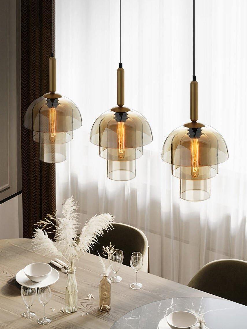 Three tiered glass pendants at staggered heights over a dining table with glasses, white plumes and curtains