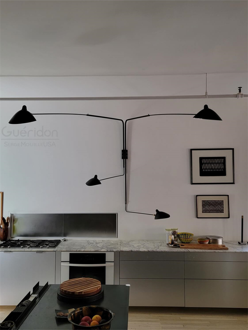 Kitchen scene with four black long-arm shades above a cooker and counter, framed art and an overhead pipe