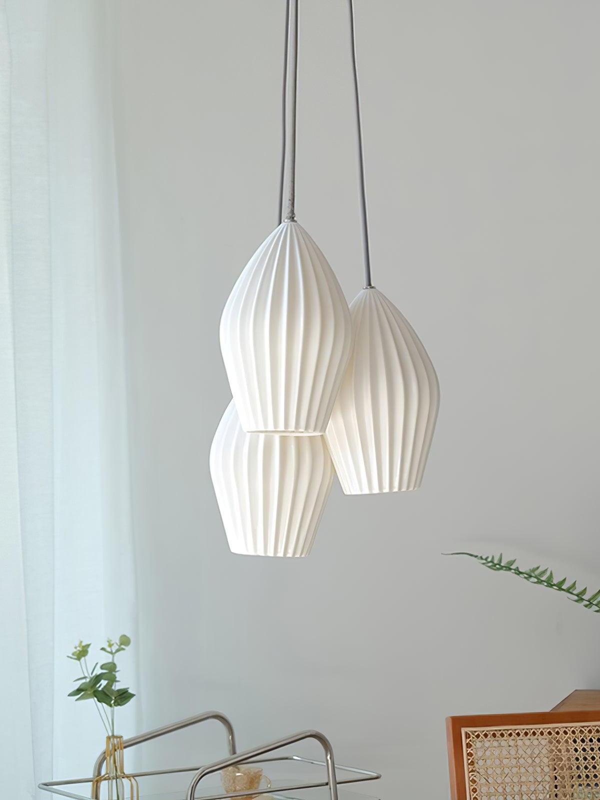 Three white ribbed pendant shades hanging at staggered heights above dining furniture