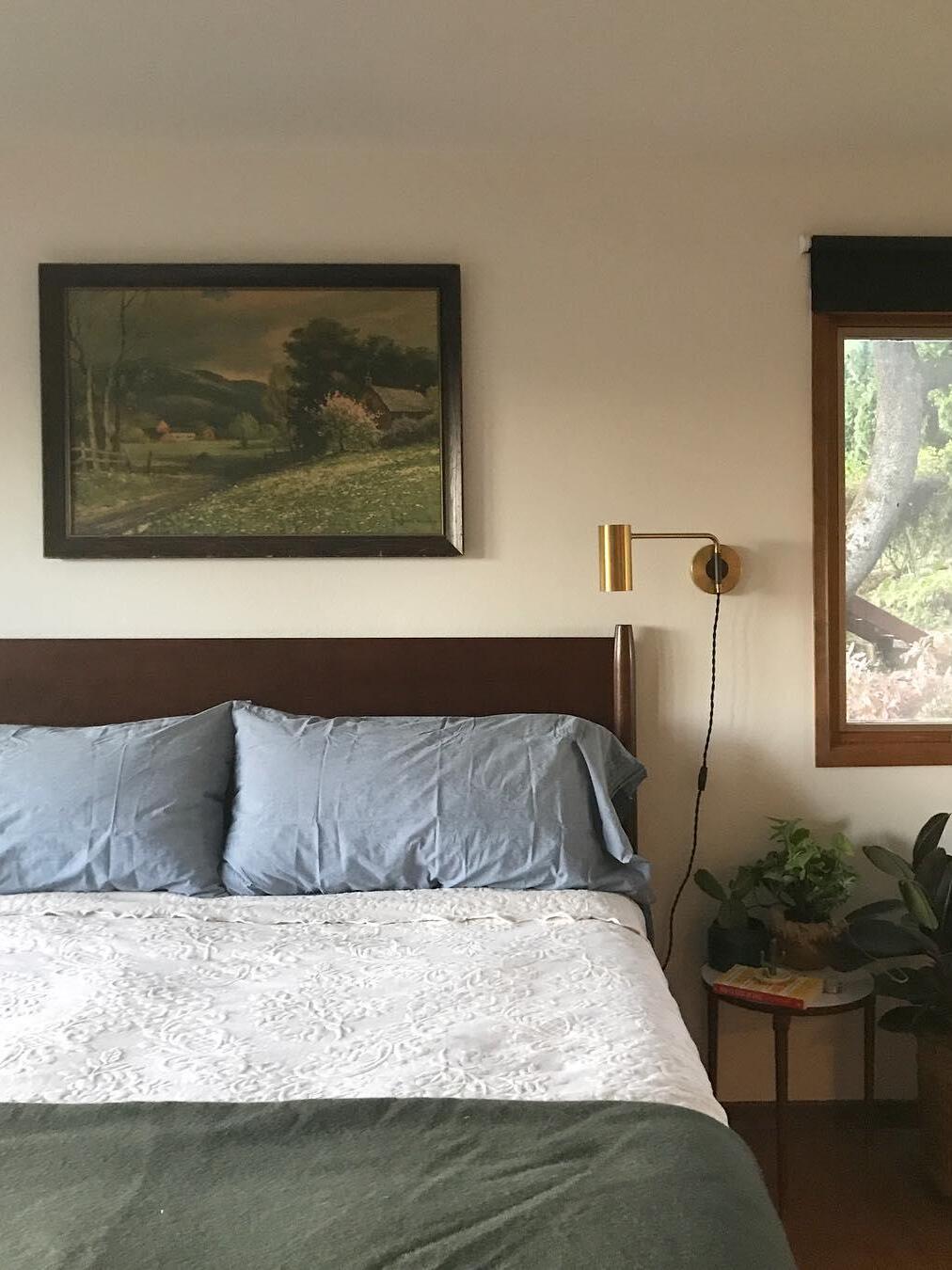 Brass-tone light beside bed near landscape art and plant