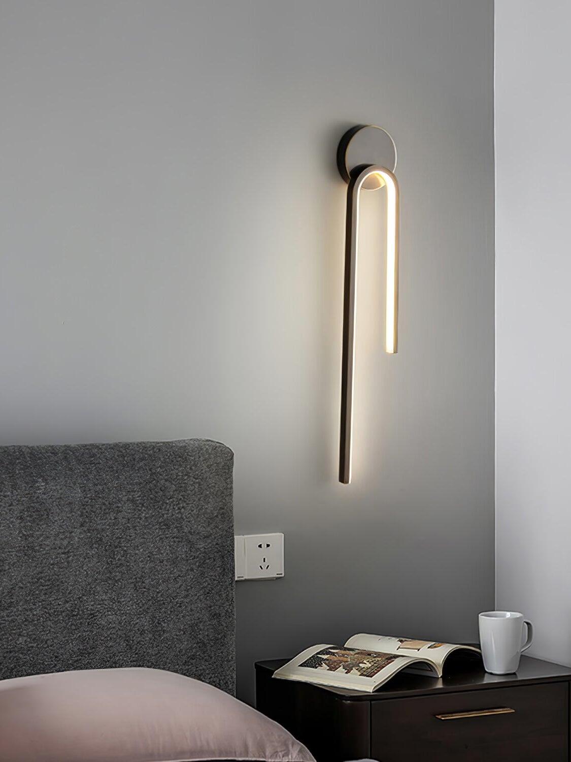 Dark arch with a long left arm beside a gray bedhead above an open book and mug on a bedside cabinet