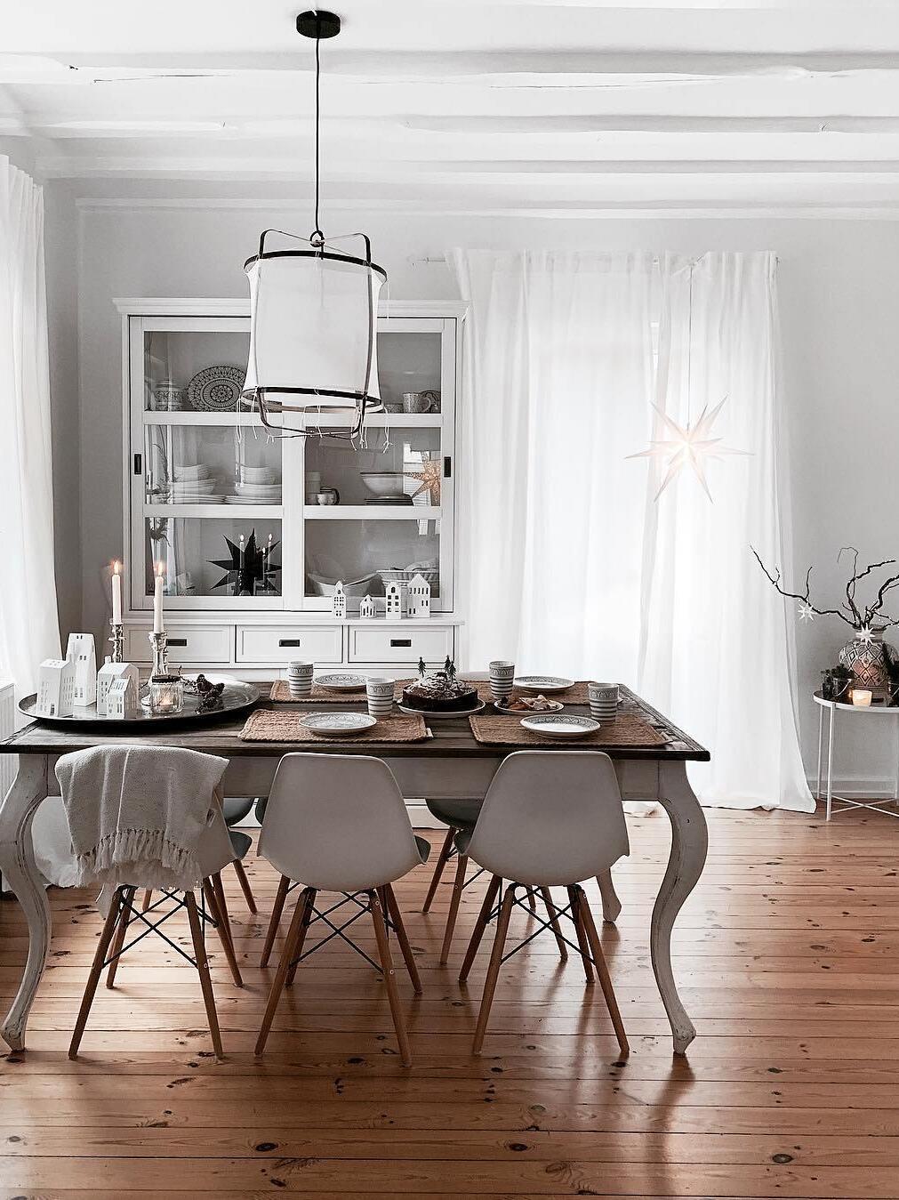 White bamboo lantern above wooden dining table with candles and tableware, white cupboard and star window decoration