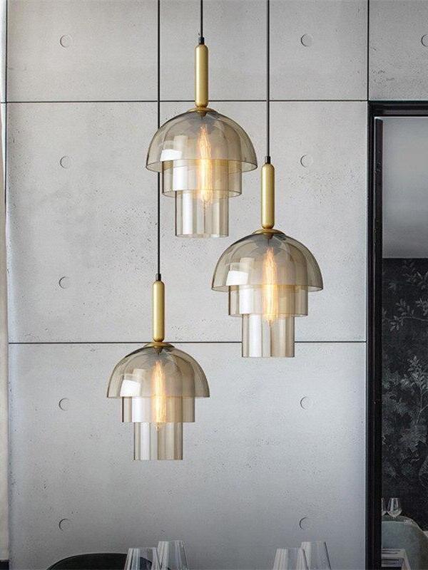 Three tiered glass pendants at staggered heights in front of a concrete-panel wall above a dining arrangement