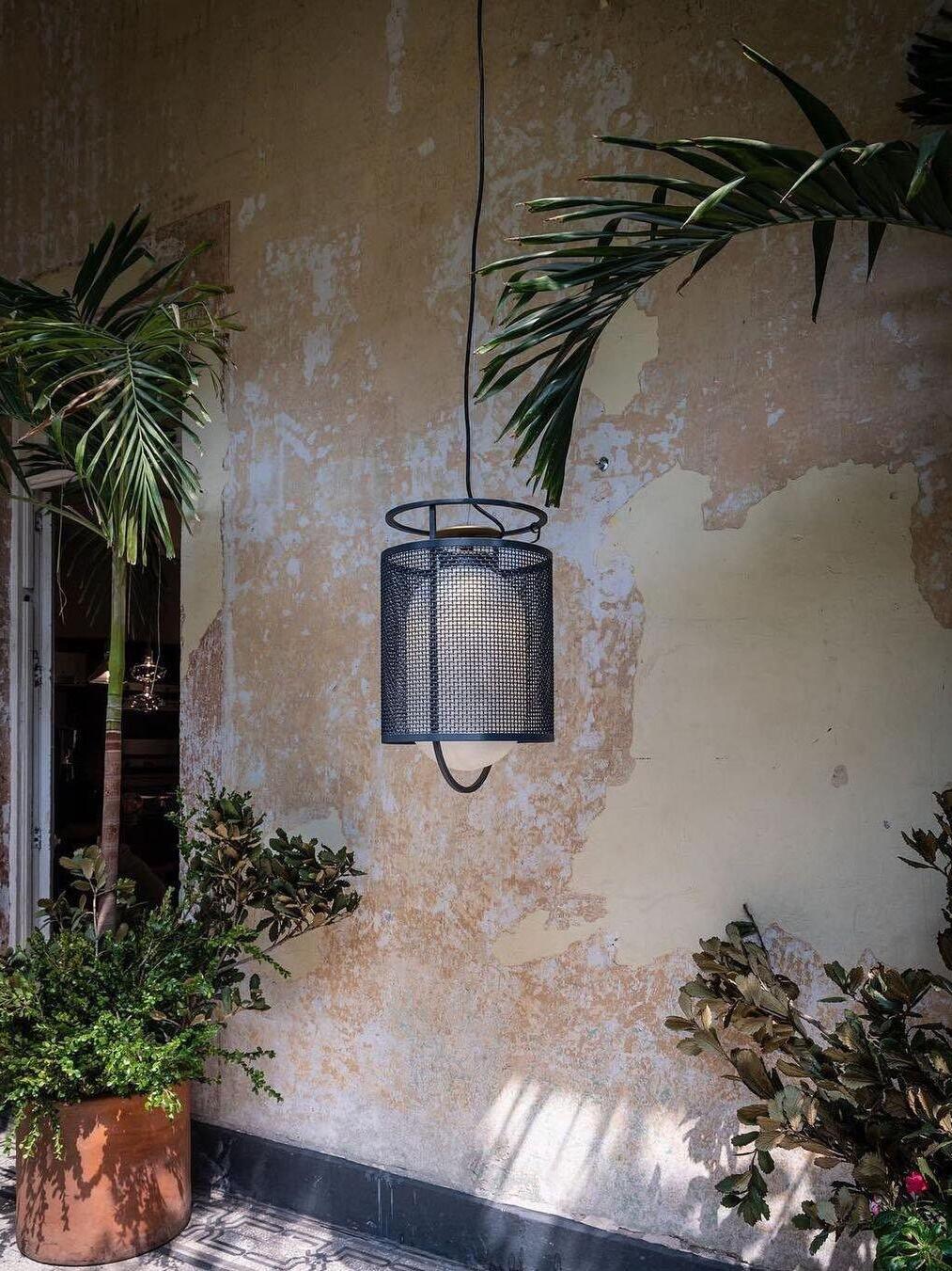 Black hanging lantern beside weathered wall and plants