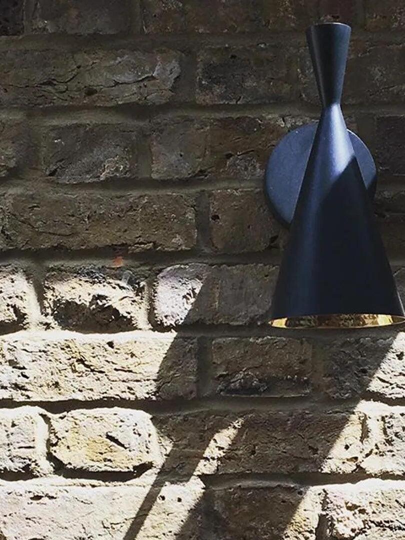 Close black conical wall light on dark brick wall