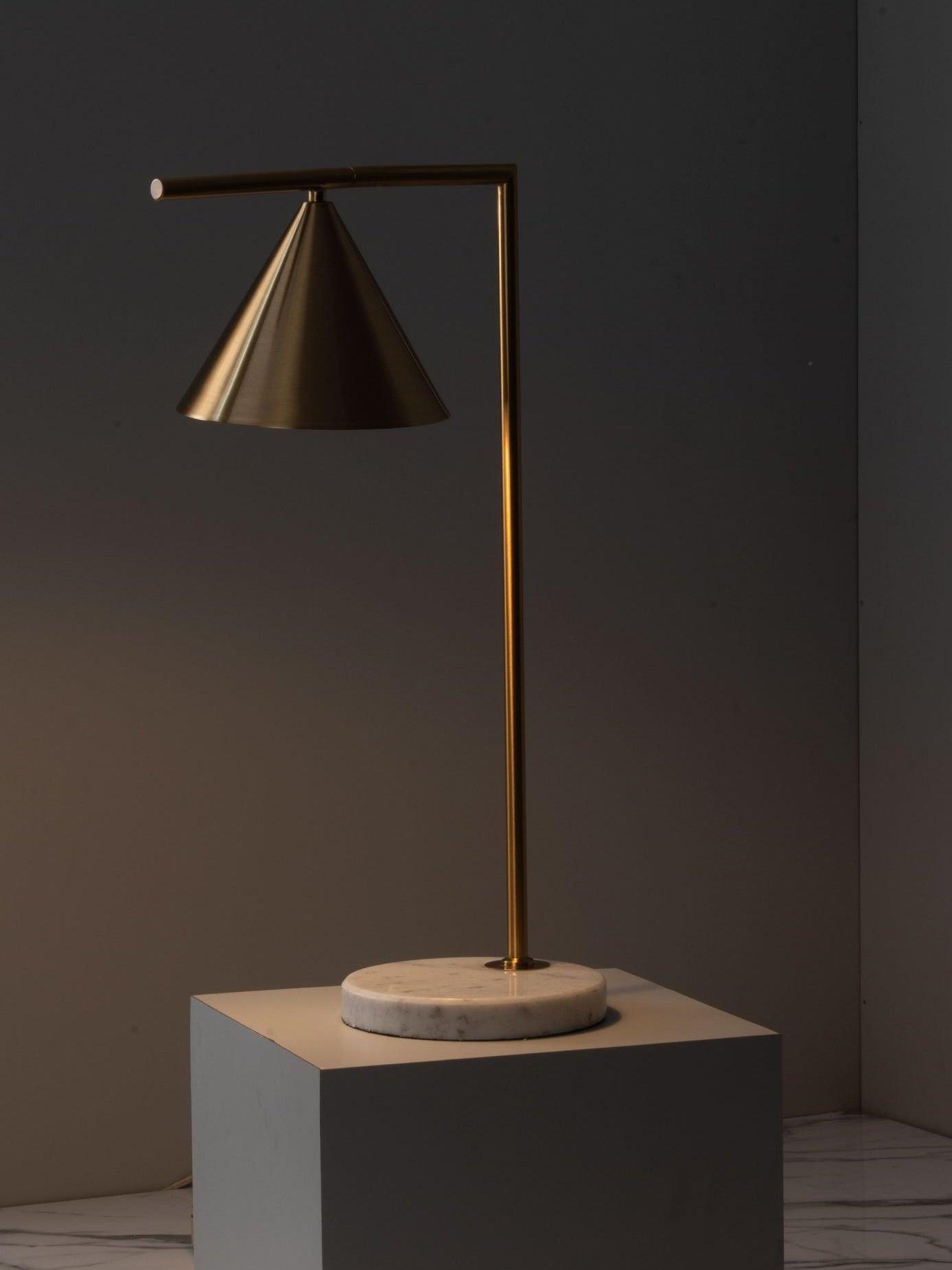 Gold-tone cone lamp illuminated on square plinth in dark room