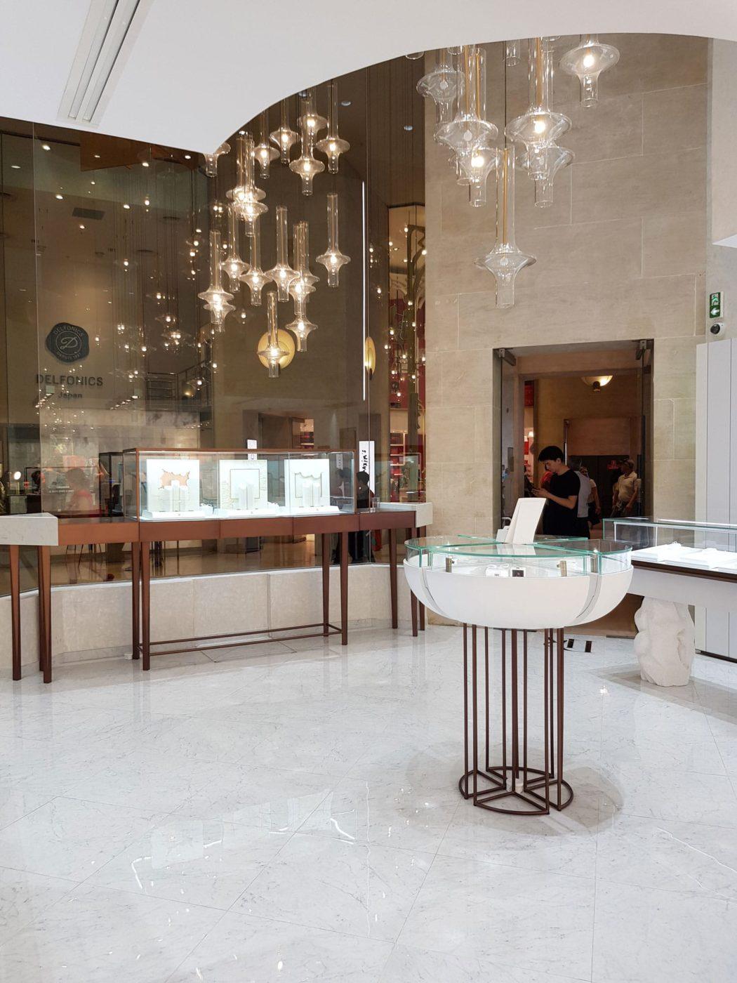 Many clear glass pendants suspended at different heights above retail display cases in a mirrored interior