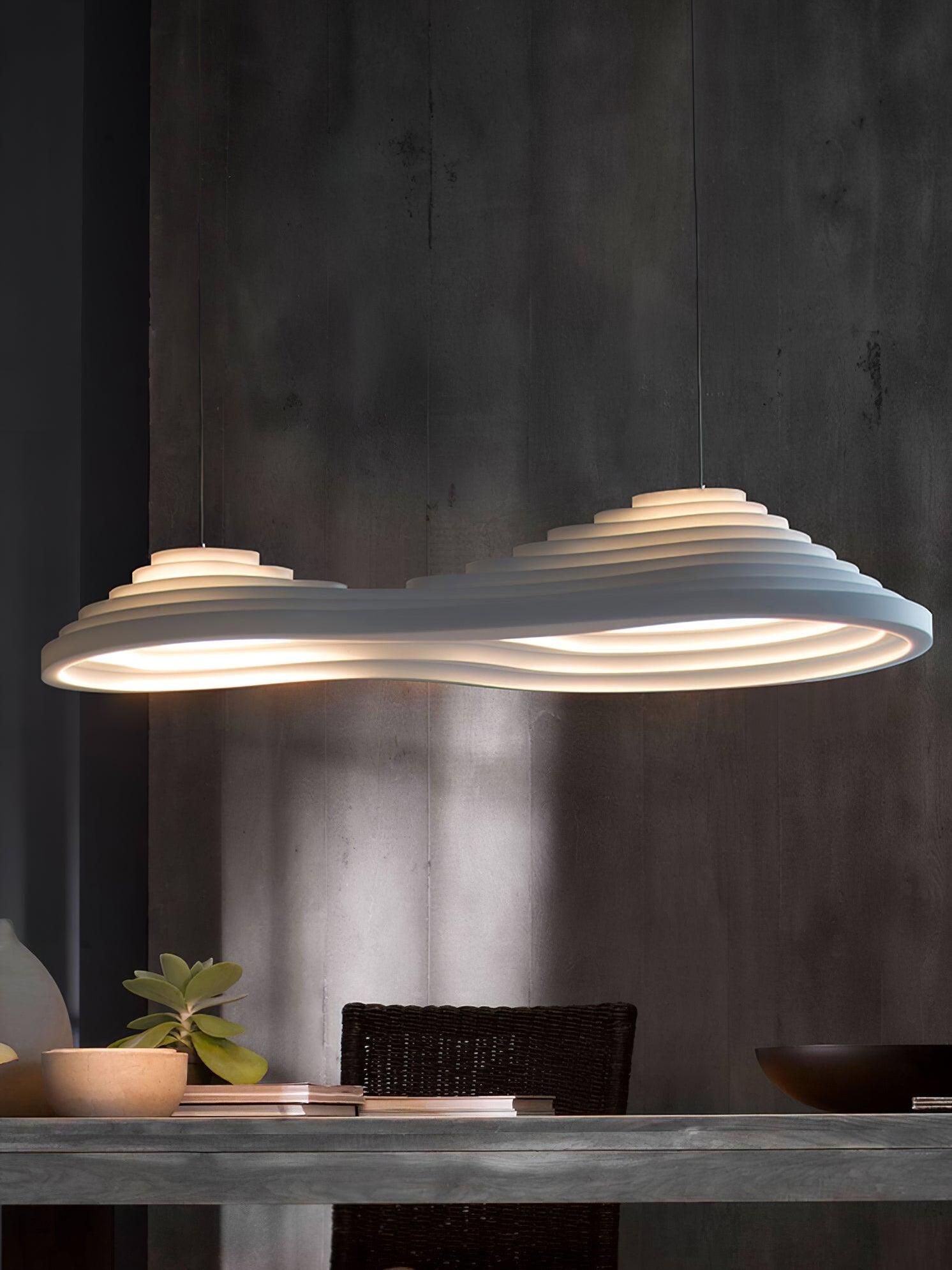 White elongated pendant with two raised sections above a table against a dark wall.