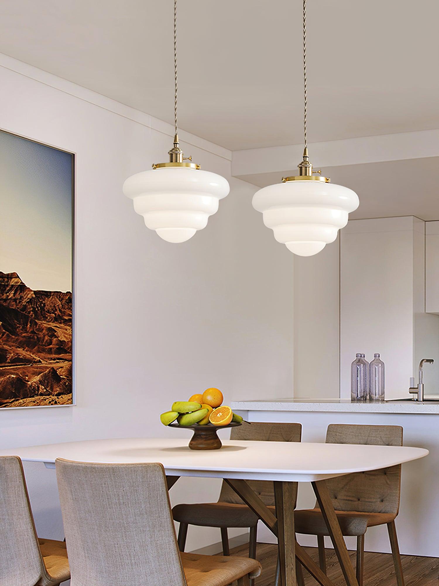 Two rounded Atlas Model B pendants above a white round table with fruit, beside a kitchen and landscape painting