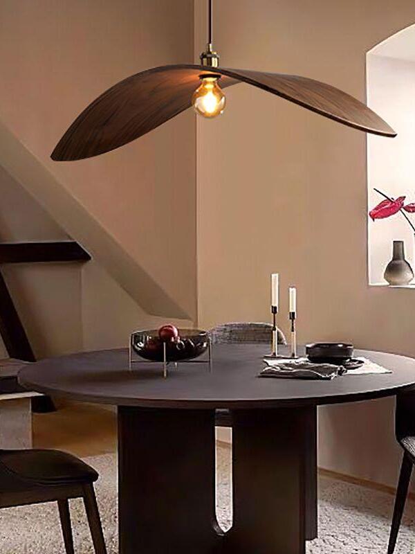 Curve wooden pendant above a round dark dining table set with glasses and candlesticks