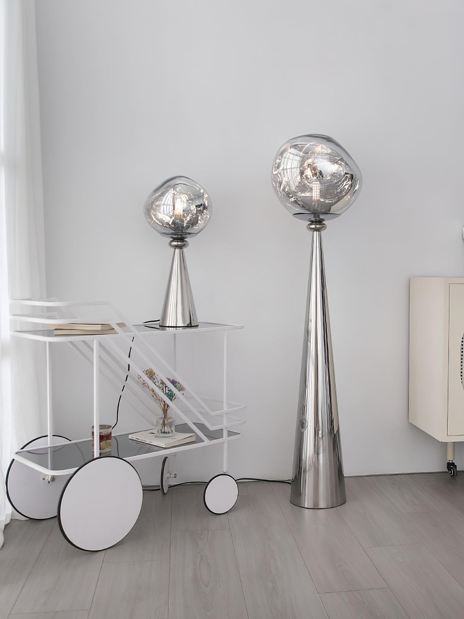 Chrome globe table lamp on a white wheeled cart beside a tall floor lamp, books and a vase