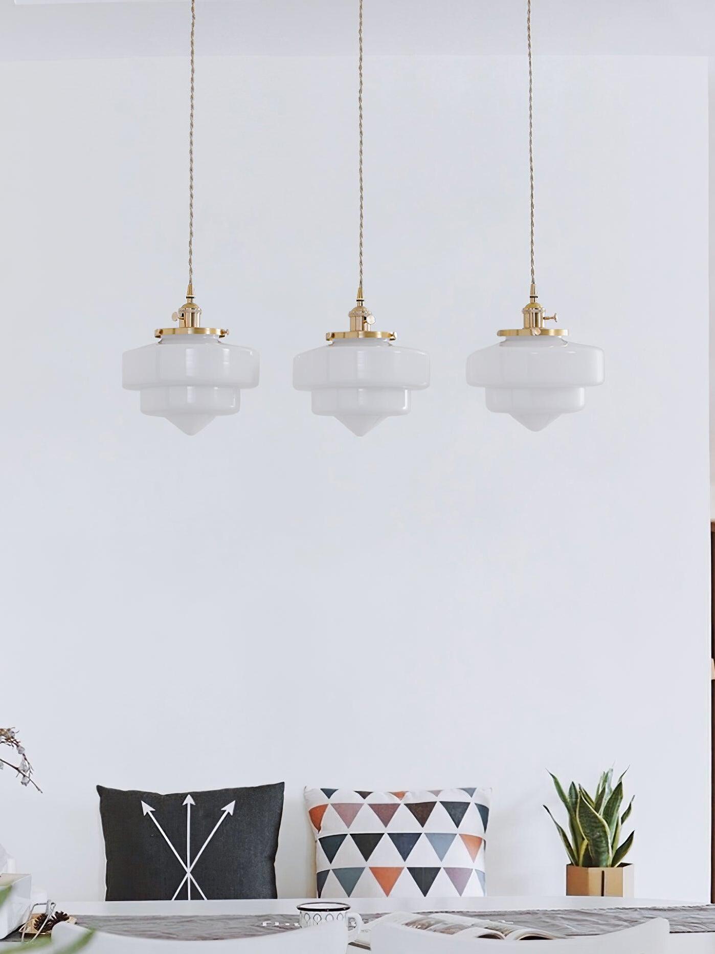 Three unlit-looking Atlas Model A shades above a bench with arrow and triangle cushions, beside a snake plant