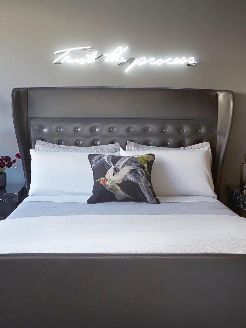 Bedroom with a dark tufted headboard, white bed and separate glowing neon lettering on the wall