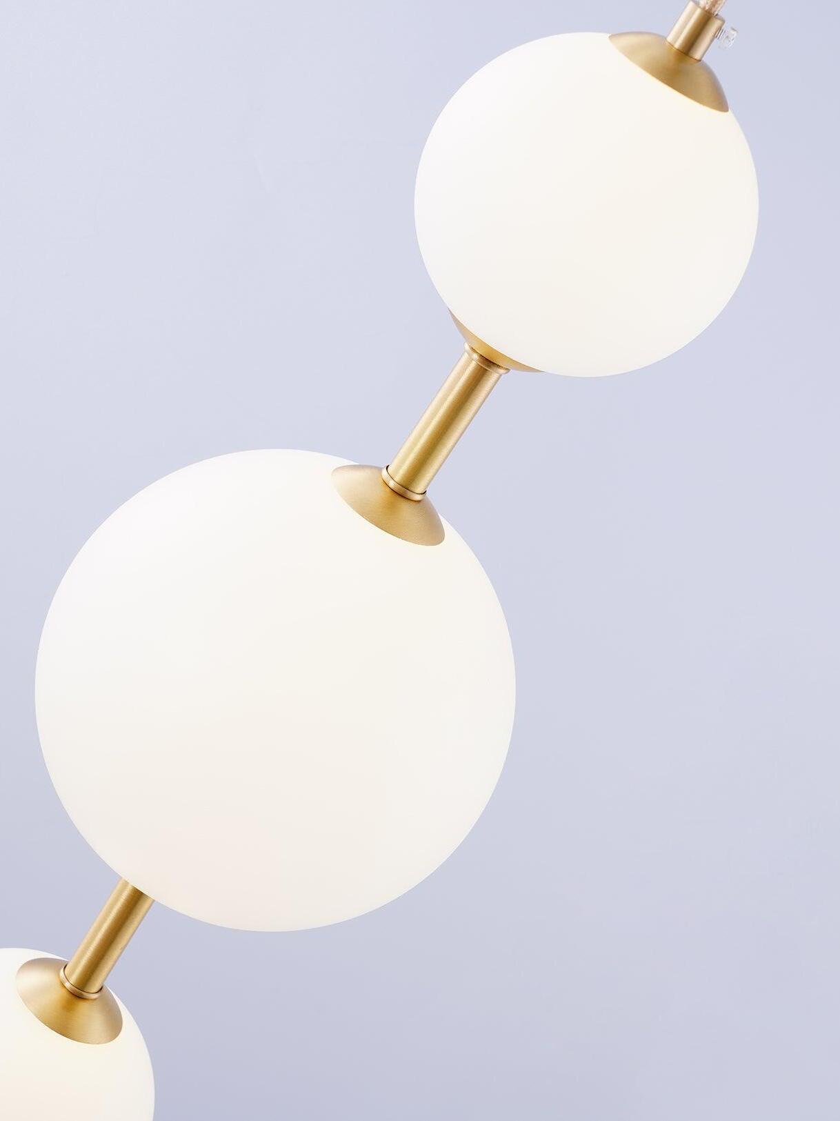 Close-up of different-size white globes joined by brass-tone collars and stems on a pale background