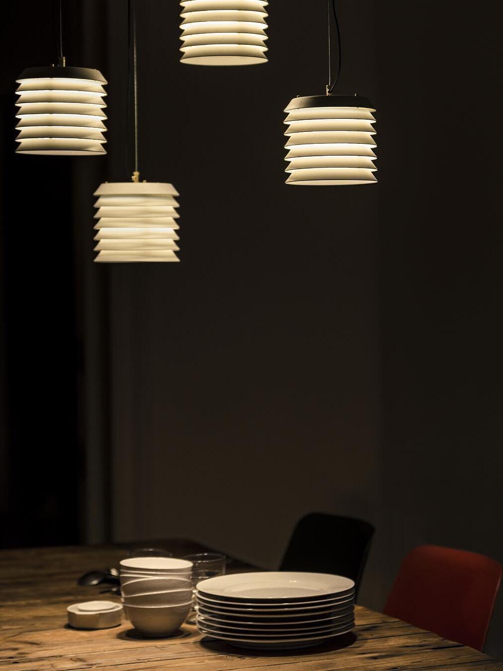 Four lit layered pendants above dining table against dark background