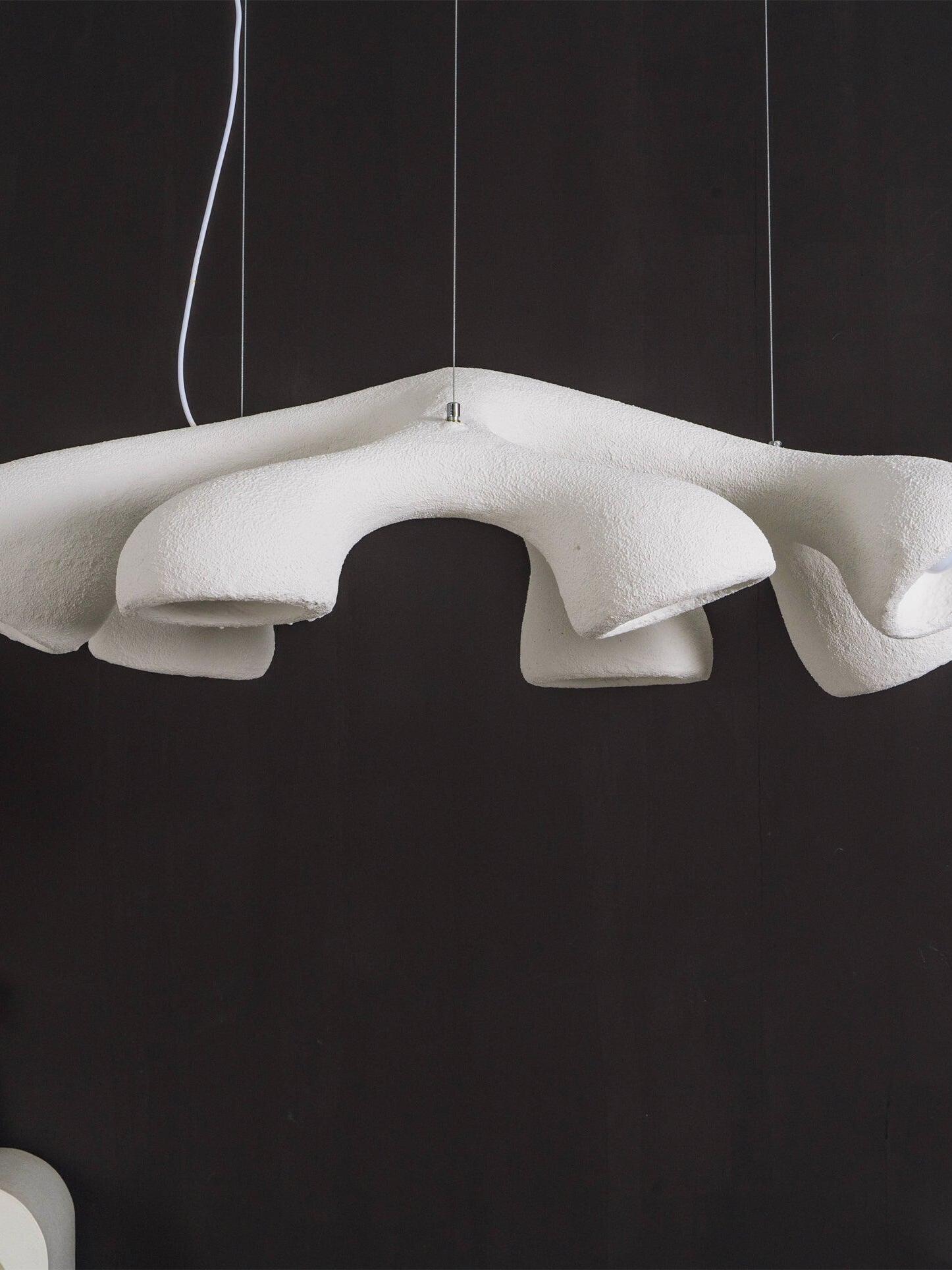 Unlit close-up of the textured white interconnected branches and bell-like outlets against a dark wall