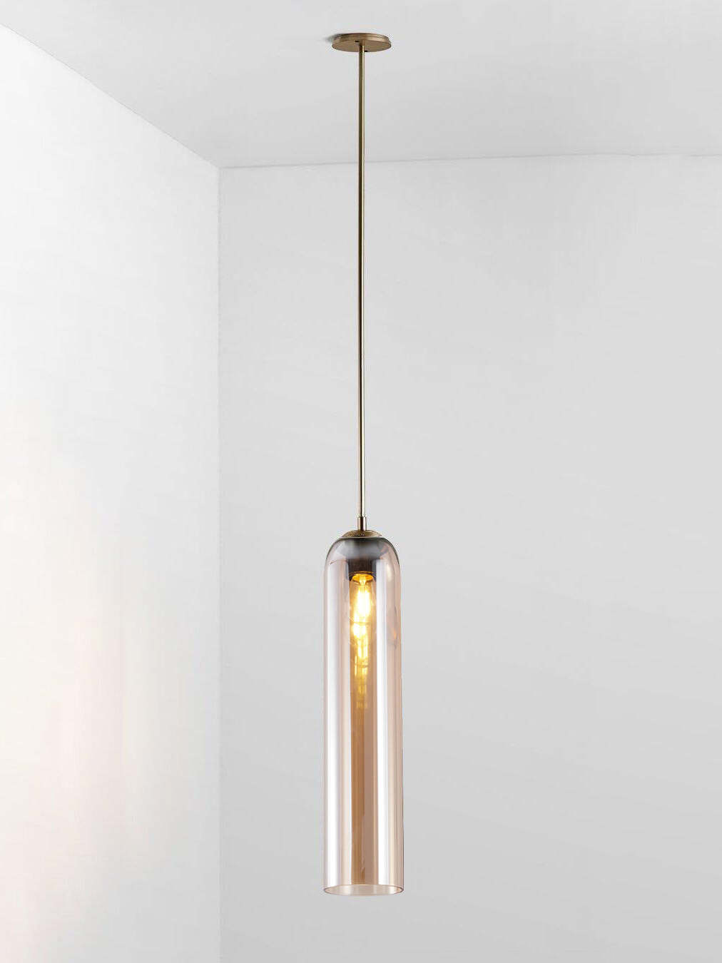 Amber glass Long Tube pendant with gold-toned rod and canopy, showing a long illuminated bulb inside the transparent shade