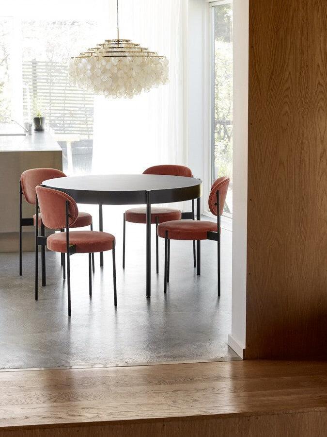 Round shell chandelier above a table with red chairs