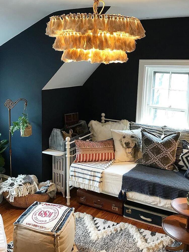 Glowing cream tassel chandelier above a daybed with patterned cushions in a dark-walled attic lounge
