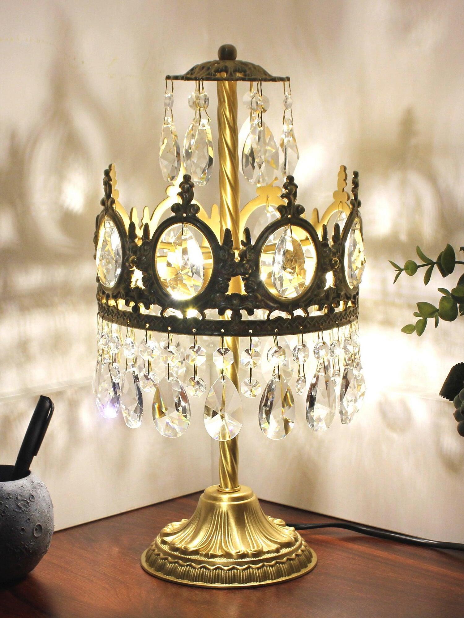 Lit crystal table lamp on a wooden surface, with crown-shaped shadows on the wall behind.