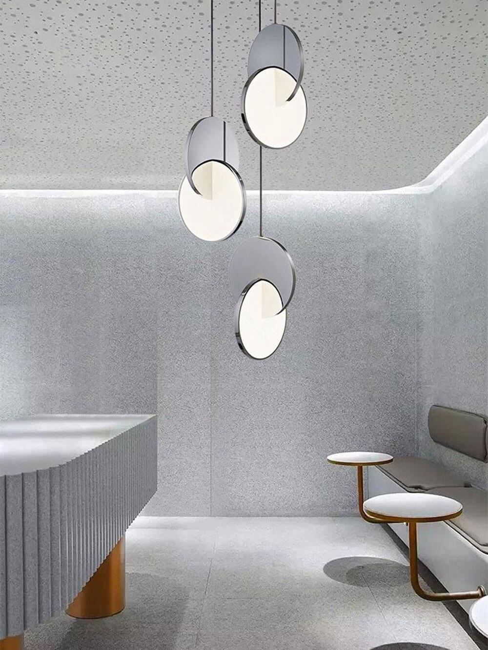 Chrome disc pendants above lounge seating and small tables beneath a perforated ceiling