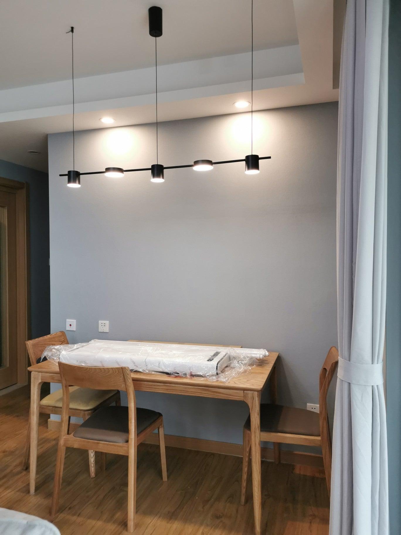Black linear fixture above a pale table near a window