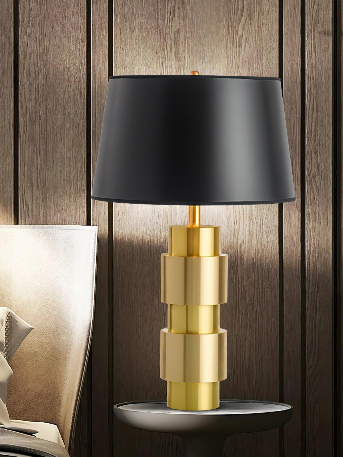Jean lamp with a black shade and gold-tone cylinders against vertical wood wall panels