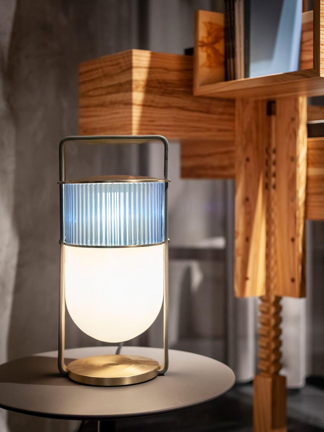 Xi lamp with lit white lower shade and pale blue-grey upper glass beside wooden wall panels