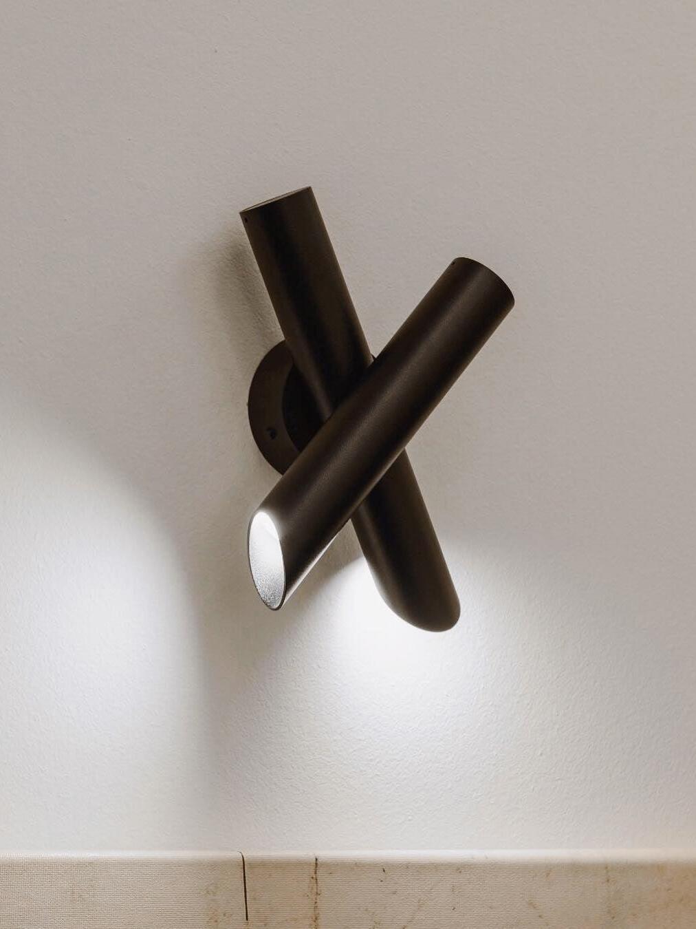 Black crossed-tube lamp and round backplate on wall